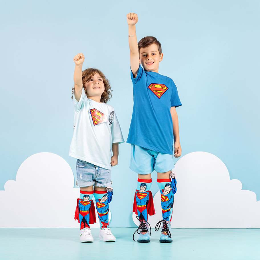 Two children in superhero-themed clothing with Superman logos on a light blue background.